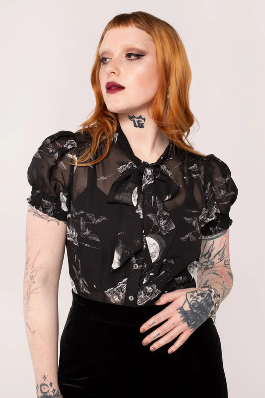 A model wearing an over the moon blouse with a black base and night sky scene, featuring short sleeves, a round neckline, and elasticated cuffs.