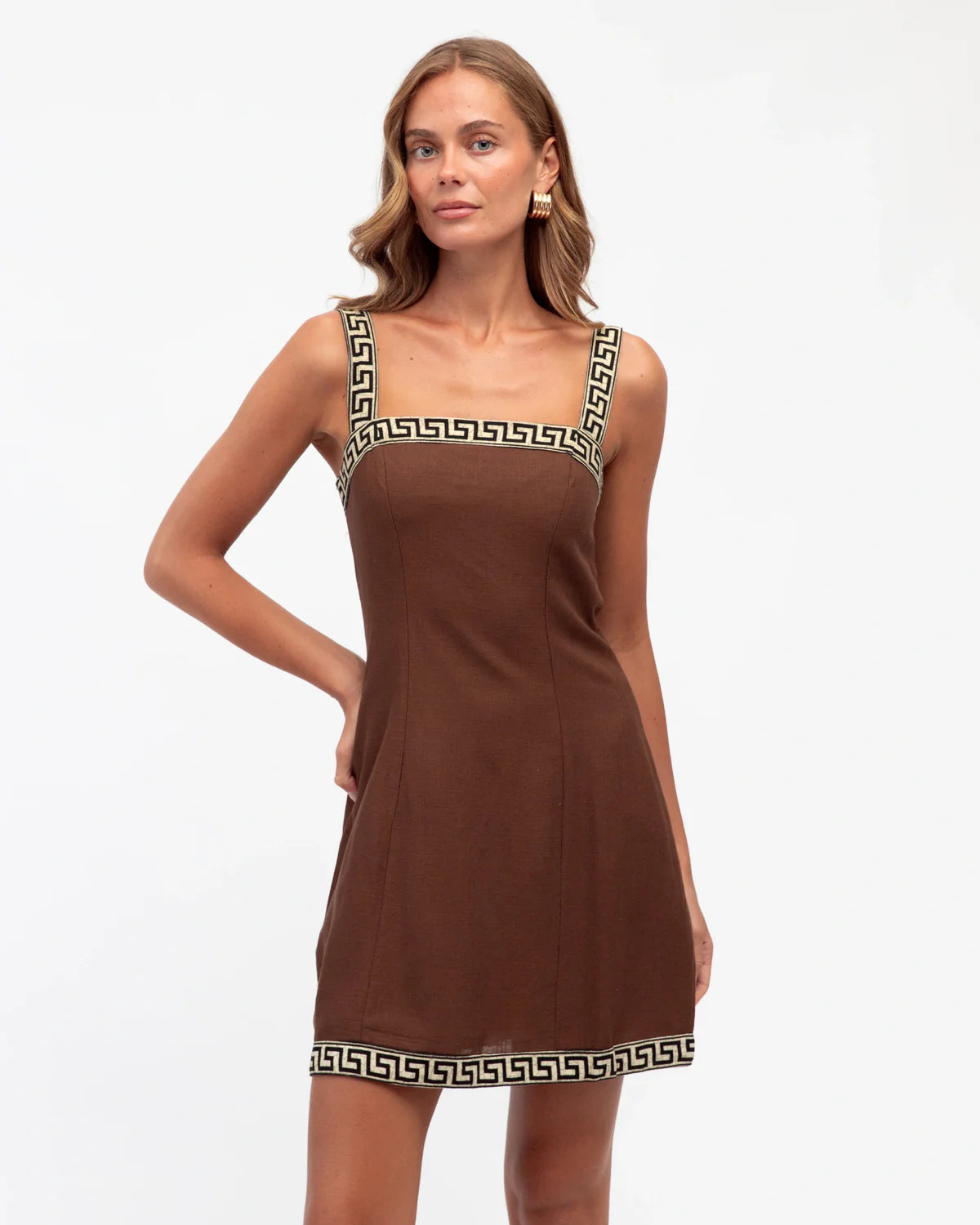 Woman wearing a brown dress with decorative straps on a white background