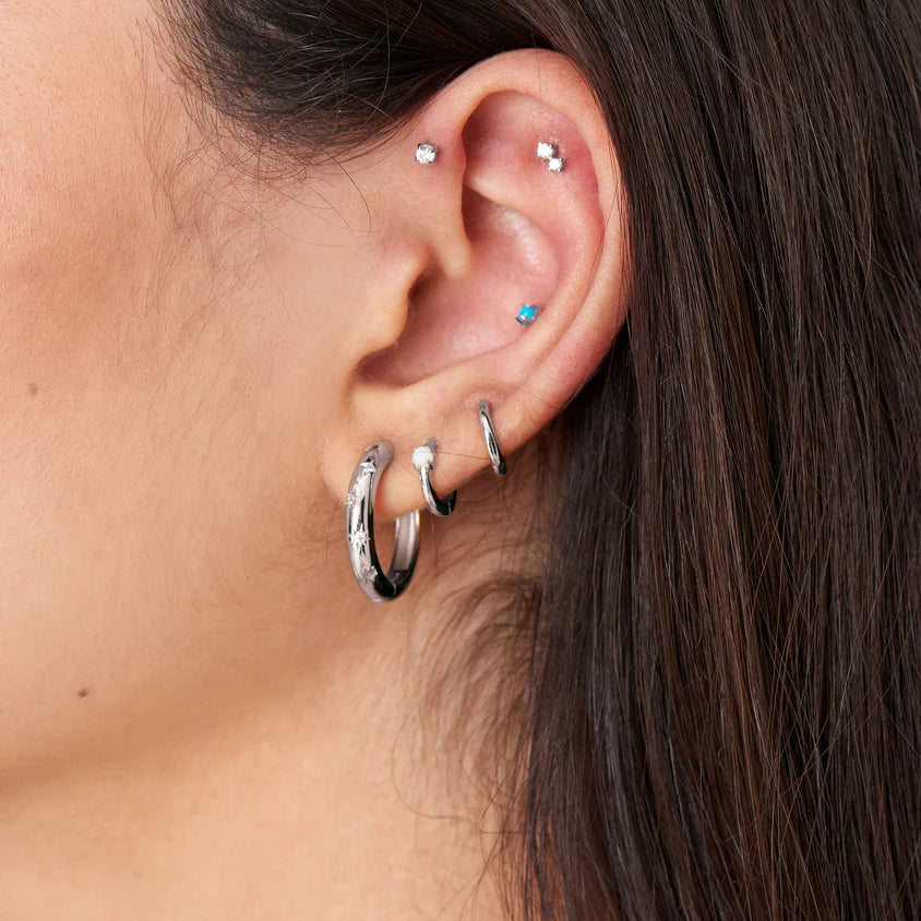 Close-up of an ear with multiple silver hoop earrings and small stud earrings.